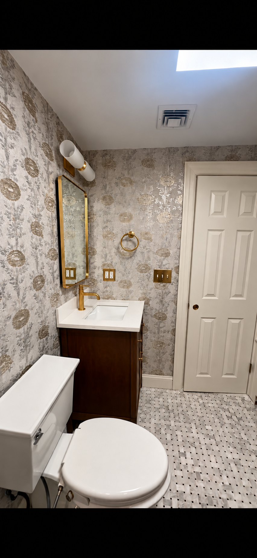 Finished bathroom with patterned wallpaper, gold fixtures and a clean vanity